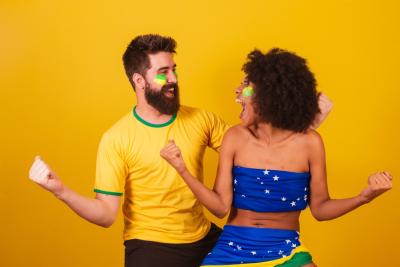 homem e mulher com as roupas da bandeira do Brasil felizes olhando um para o outro em um fundo amarelo-casal torcedor-Assaí Atacadista