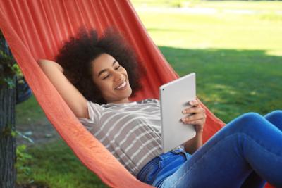 jovem negra descansando em uma rede com um tablet na mão - descansar nas férias - Assaí Atacadista