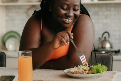 mulher negra feliz com um garfo olhando para um prato de comida - Assaí Atacadista - equilíbrio