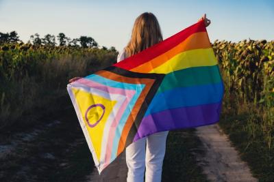 pessoa de costas segurando a bandeira LGBTQIA+ em um campo - diversidade no Assaí Atacadista
