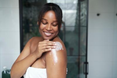  mulher negra sorrindo passando hidratante na pele-temporada de hidratação-Nivea-Assaí Atacadista