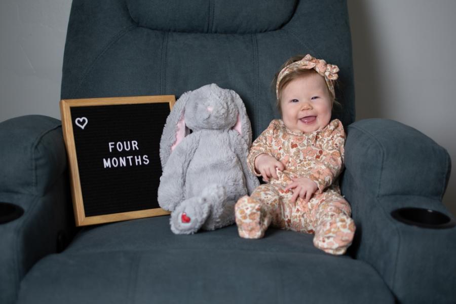 bebe branca sorrindo em uma poltrona com um ursinho e uma placa-Assaí Atacadista-Mesversário