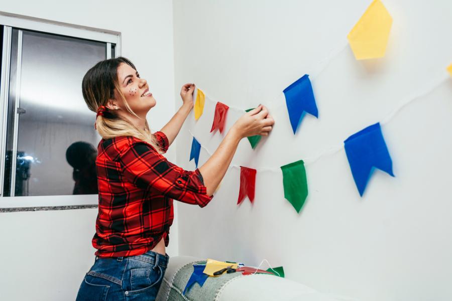 mulher branca colocando decoração de festa junina na parede - Assaí Atacadista