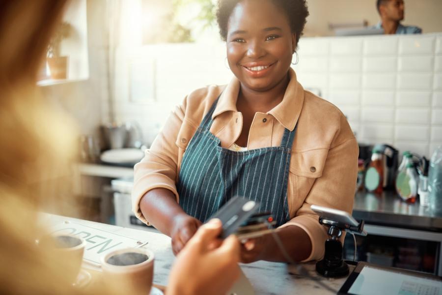 moça negra sorrindo recebendo o pagamento de uma compra em um comércio - Mês do Comerciante - Assaí Atacadista