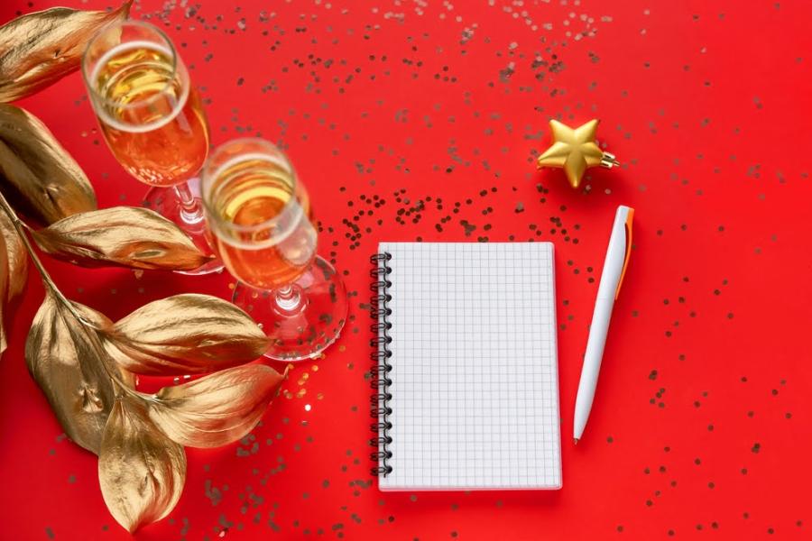 fundo vermelho com taças de champanhe e um bloco de notas em branco com uma caneta - resoluções de Ano-Novo - Assaí Atacadista
