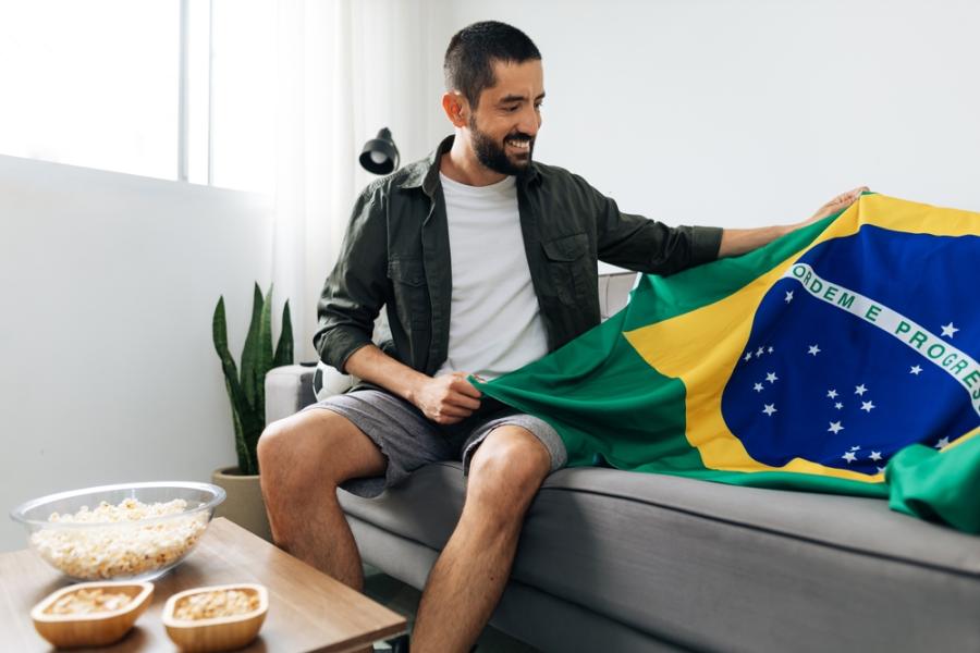 homem branco segurando uma bandeira do Brasil em um sofá-brasilcore junino-Assaí Atacadista