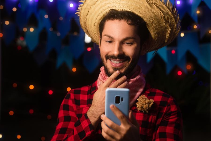 homem com trajes juninos segurando celular - prestação de serviços juninos - Assaí Atacadista