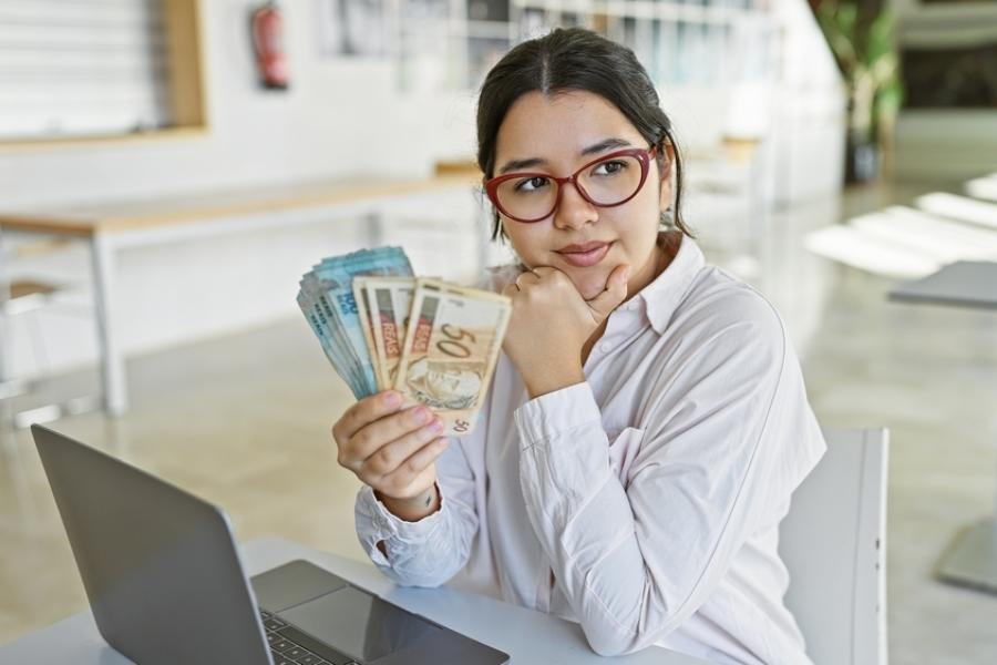 jovem brasileira com notas de dinheiro na mão - decisões financeiras - Assaí Atacadista