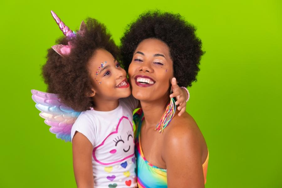 mãe e filha negras felizes com roupas e acessórios de carnaval em um fundo verde - carnaval com crianças - Assaí Atacadista