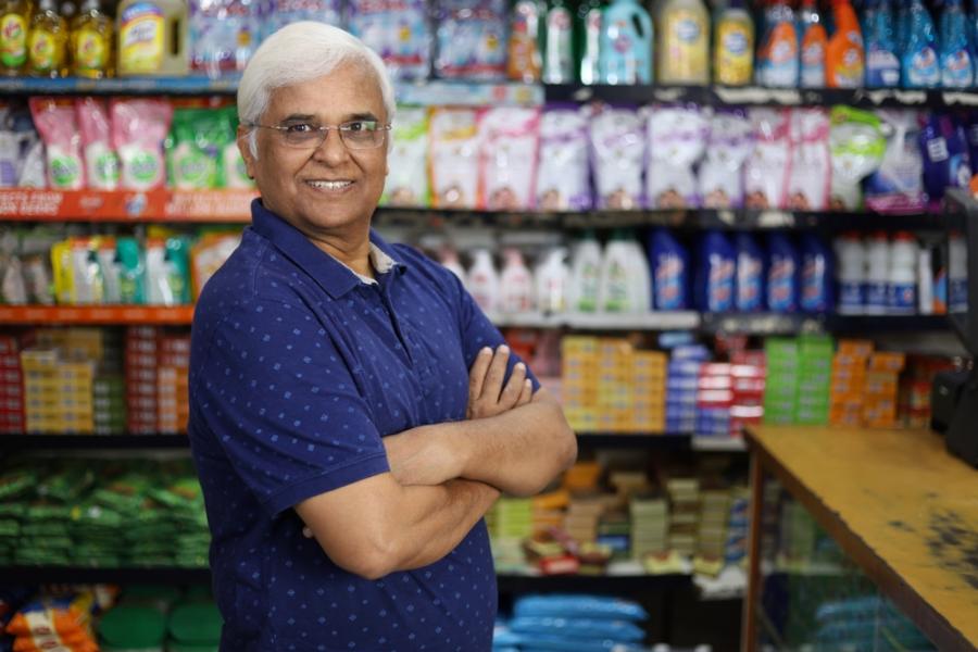 homem idoso com os braços cruzados em um comércio - Mês do Comerciante - Assaí Atacadista