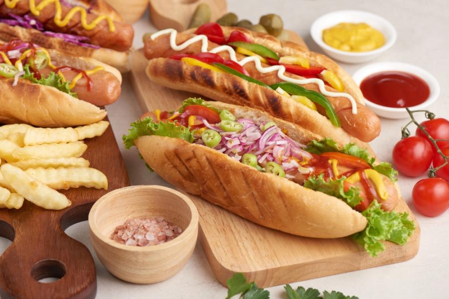 mesa com dois cachorros quentes em um tábua com condimentos batatas e outros ingredientes - Assaí Atacadista - cachorro-quente