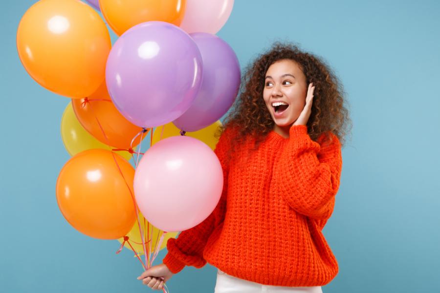 mulher feliz segurando bexigas laranjas rosas e roxas em um fundo azul - Assaí Atacadista - aniversário sem festa