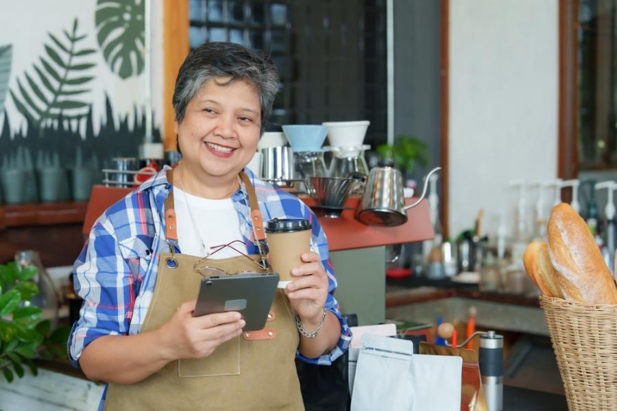 mulher idosa empreendedora feliz segurando um café e um tablet-Assaí Atacadista