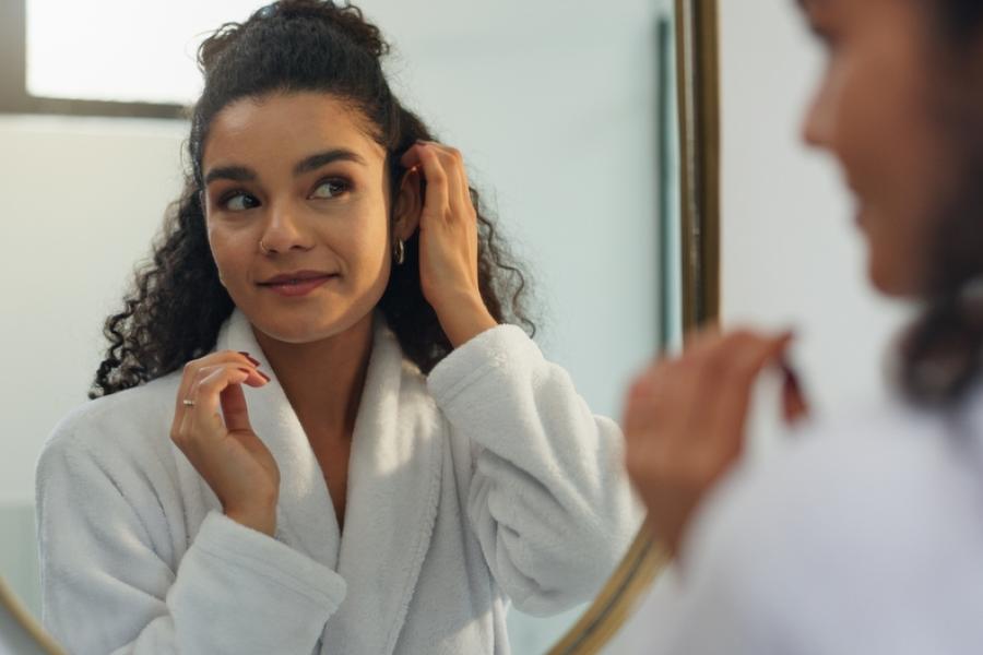 mulher negra feliz de roupão branco se olhando no espelho-autocuidado acessível-Assaí Atacadista