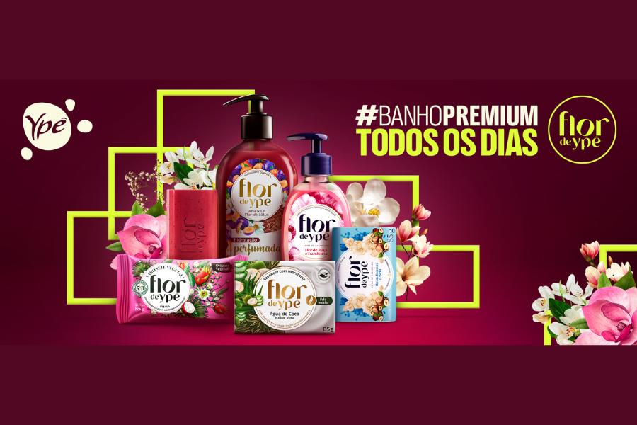 Uma seleção de diversos sabonetes em barra , sabonetes líquidos e hidratantes da marca Flor de Ypê sobre um fundo rosa escuro. Na imagem, a frase “Banho premium todos os dias” acompanhada por uma hashtag.