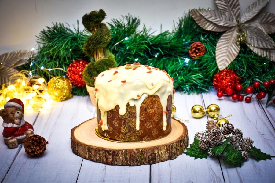 panetone com cobertura branca em um suporte com o fundo cheio de decorações natalinas - Assaí Atacadista - panetone artesanal