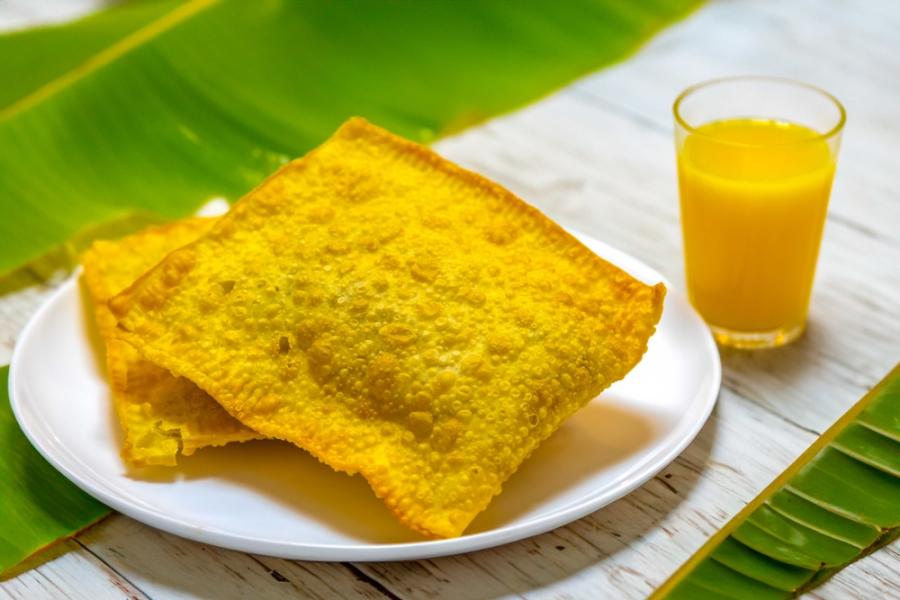 prato com dois pastéis de feira e um suco da cor laranja em um copo em uma mesa com folhas de bananeira - snacks de carnaval - Assaí Atacadista - Imagem Shutterstock