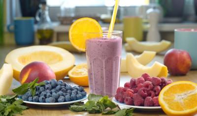 copo com bebida roxa e fatia de laranja na borda em uma mesa com frutas diversas - smoothies energéticos - Assaí Atacadista