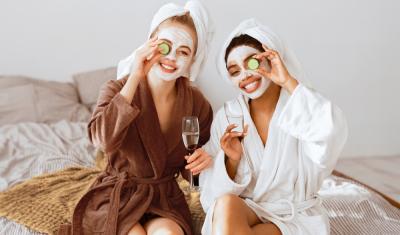 duas mulheres felizes em roupão e máscara facial segurando um copo e uma rodela de pepino nas mãos - spa em casa - Assaí Atacadista