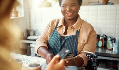 moça negra sorrindo recebendo o pagamento de uma compra em um comércio - Mês do Comerciante - Assaí Atacadista