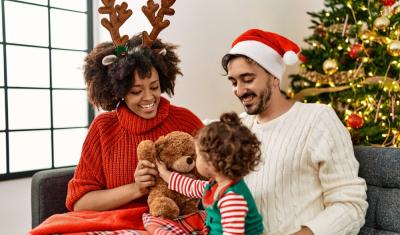 familia feliz com mulher negra homem branco e bebe com trajes de natal e uma arvore de natal no fundo - Assaí Atacadista - final de ano