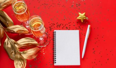 fundo vermelho com taças de champanhe e um bloco de notas em branco com uma caneta - resoluções de Ano-Novo - Assaí Atacadista