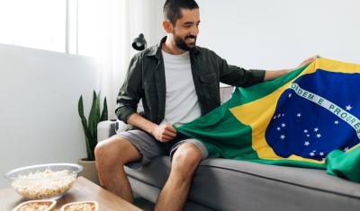 homem branco segurando uma bandeira do Brasil em um sofá-brasilcore junino-Assaí Atacadista