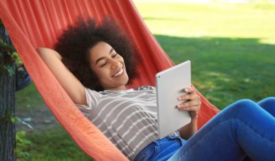 jovem negra descansando em uma rede com um tablet na mão - descansar nas férias - Assaí Atacadista