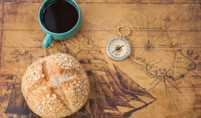 mapa antigo com pão, xícara de café e um compasso em cima - Assaí Atacadista - dia do pão