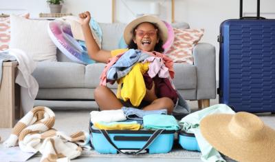 menina negra feliz segurando roupas em uma mala de viagem - destinos de viagem verão - Assaí Atacadista