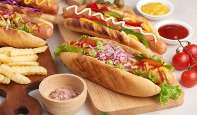 mesa com dois cachorros quentes em um tábua com condimentos batatas e outros ingredientes - Assaí Atacadista - cachorro-quente