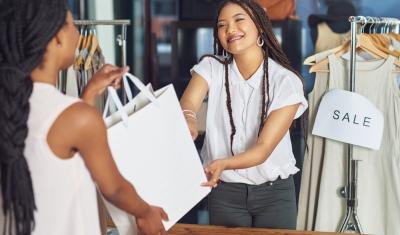 moça sorrindo entregando uma sacola para uma cliente em uma loja de roupas - Assaí Atacadista - atendimento ao cliente