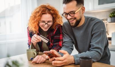 mulher e homem brancos apoiados em uma bancada olhando para o celular felizes - Dia do Consumidor - Assaí Atacadista - Imagem: Shutterstock