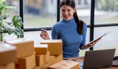 mulher empreendedora asiatica olhando para caixas na mesa - franquias populares - Assaí Atacadista