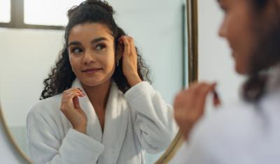 mulher negra feliz de roupão branco se olhando no espelho-autocuidado acessível-Assaí Atacadista