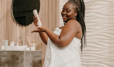 mulher negra feliz de toalha em um banheiro passando hidratante nas mãos-produtos Dove-Assaí Atacadista