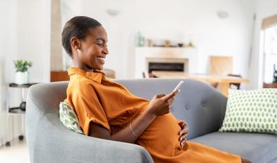 mulher negra sorrindo segurando um celular sentada no sofá-Assaí no Ifood-Assaí Atacadista