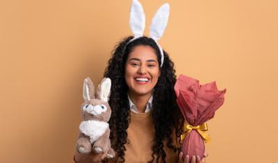 mulher sorridente com orelhas de coelho segurando um coelho de pelucia e um ovo de chocolate nas mãos - presente para o dia da mulher - assaí atacadista