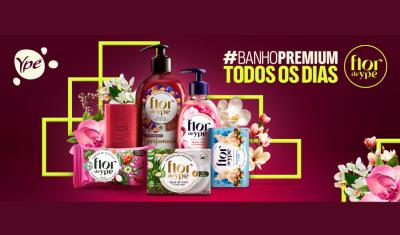 Uma seleção de diversos sabonetes em barra , sabonetes líquidos e hidratantes da marca Flor de Ypê sobre um fundo rosa escuro. Na imagem, a frase “Banho premium todos os dias” acompanhada por uma hashtag.