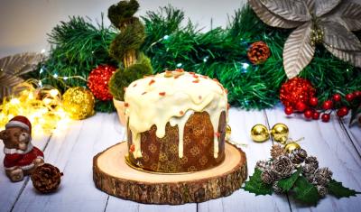 panetone com cobertura branca em um suporte com o fundo cheio de decorações natalinas - Assaí Atacadista - panetone artesanal