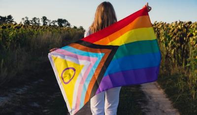 pessoa de costas segurando a bandeira LGBTQIA+ em um campo - diversidade no Assaí Atacadista