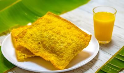 prato com dois pastéis de feira e um suco da cor laranja em um copo em uma mesa com folhas de bananeira - snacks de carnaval - Assaí Atacadista - Imagem Shutterstock