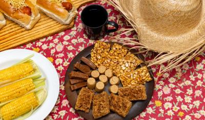 pratos com comidas típicas de São João e um chapéu de palha em uma toalha floral - Assaí Atacadista