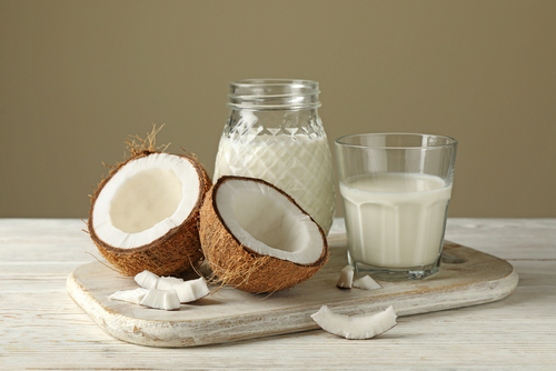 tábua com coco partido ao meio e um copo com leite de coco - bebidas vegetais - Assaí Atacadista