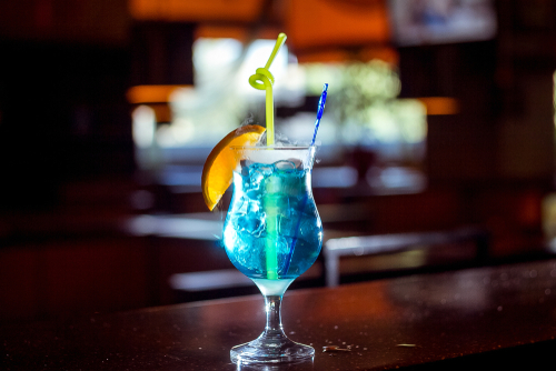 taça com drink azul, gelo e canudinhos em uma bancada de bar - bebidas sem álcool - Assaí Atacadista - Imagem: Shutterstock