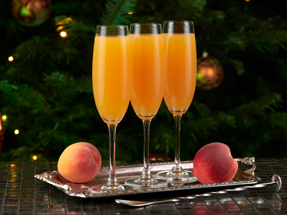 taça com drink de pêssego acompanhado de dois pêssegos e uma árvore de Natal no fundo - Assaí Atacadista - drinks de Natal