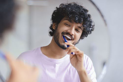 homem jovem escovando os dentes olhando no espelho-creme dental Sensodyne-Assaí Atacadista