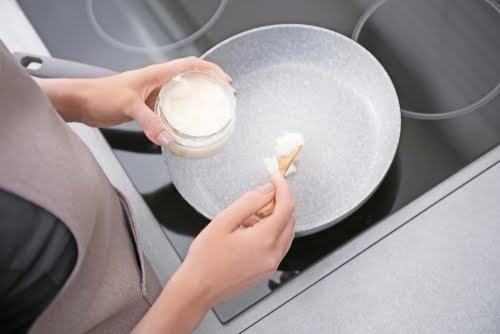 pessoa branca colocando uma colher de óleo de coco em uma panela-Assaí Atacadista-Coco & Cia